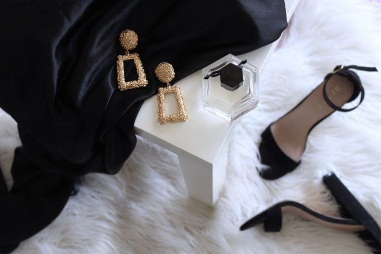 Affordable Luxury - pair of gold-colored earrings on table and black ankle-strap pumps on area rug