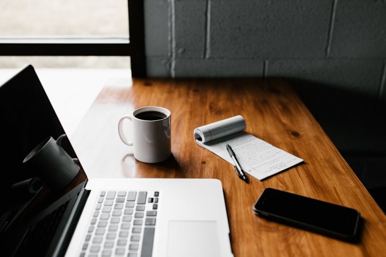 Tech Luxury - MacBook Pro, white ceramic mug,and black smartphone on table